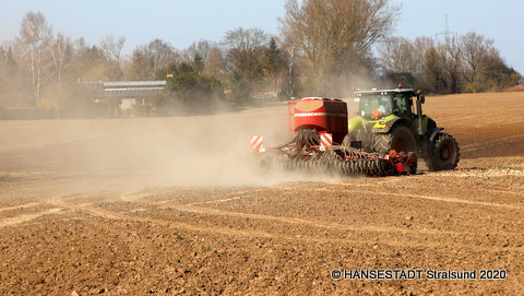 Der Traktor mit angehängter Drillmaschine zieht auf dem Acker seine Runden und bringt hier eine Mischung mit Kräutern und Blumen in den Boden